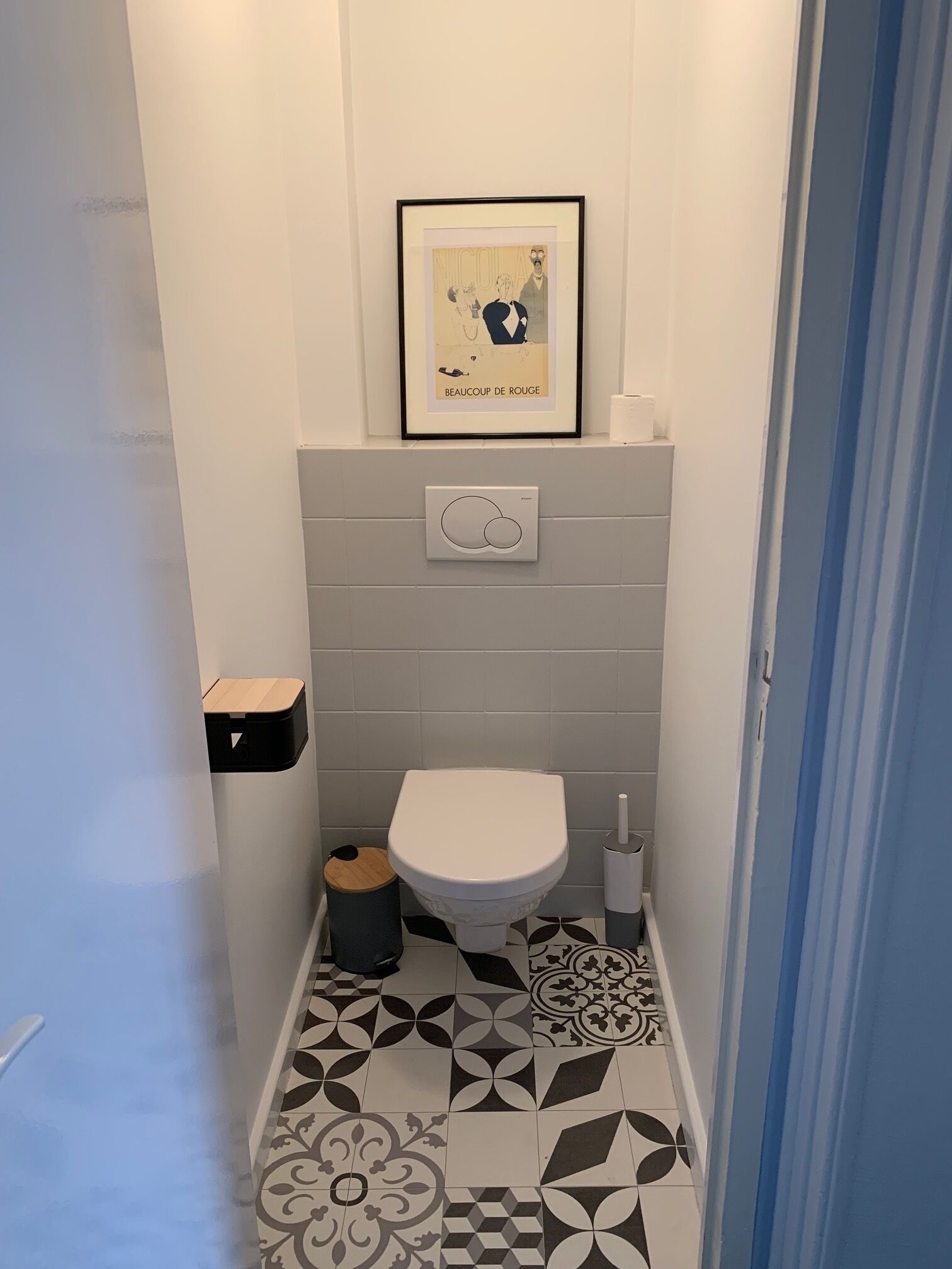 A small bathroom with a toilet, a trash bin, and a framed picture on the wall.
