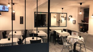 A restaurant interior with multiple tables and chairs, a large mirror, and hanging pendant lights. - Hôtel L'ESTRAN (Trouville-sur-Mer)