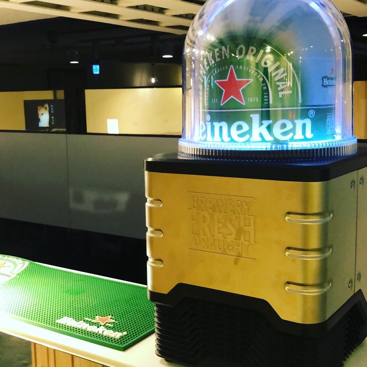 A Heineken beer bottle on a metallic stand with embossed text.