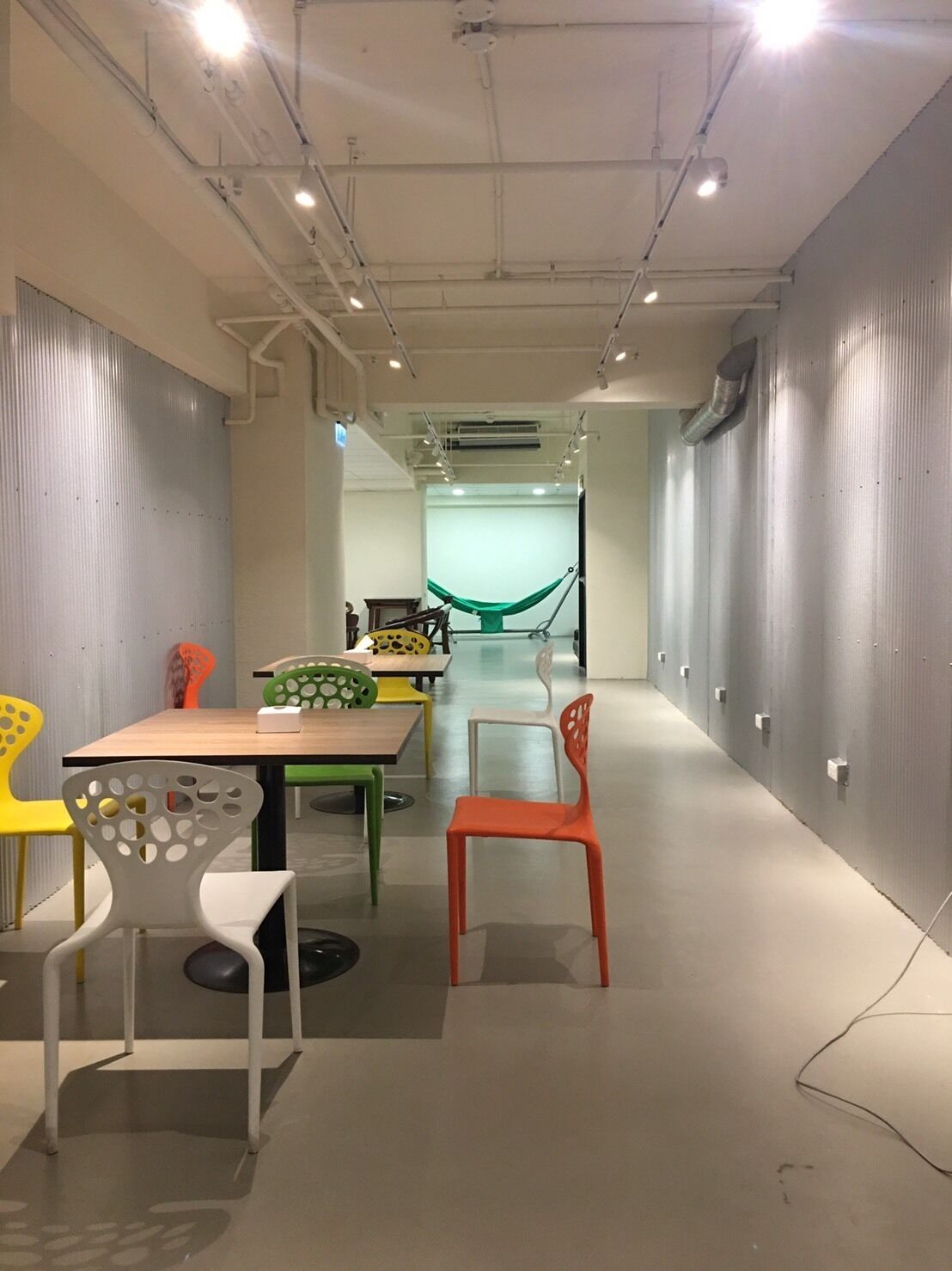 A conference room with a long table and colorful chairs, a hammock, and a view into another room.