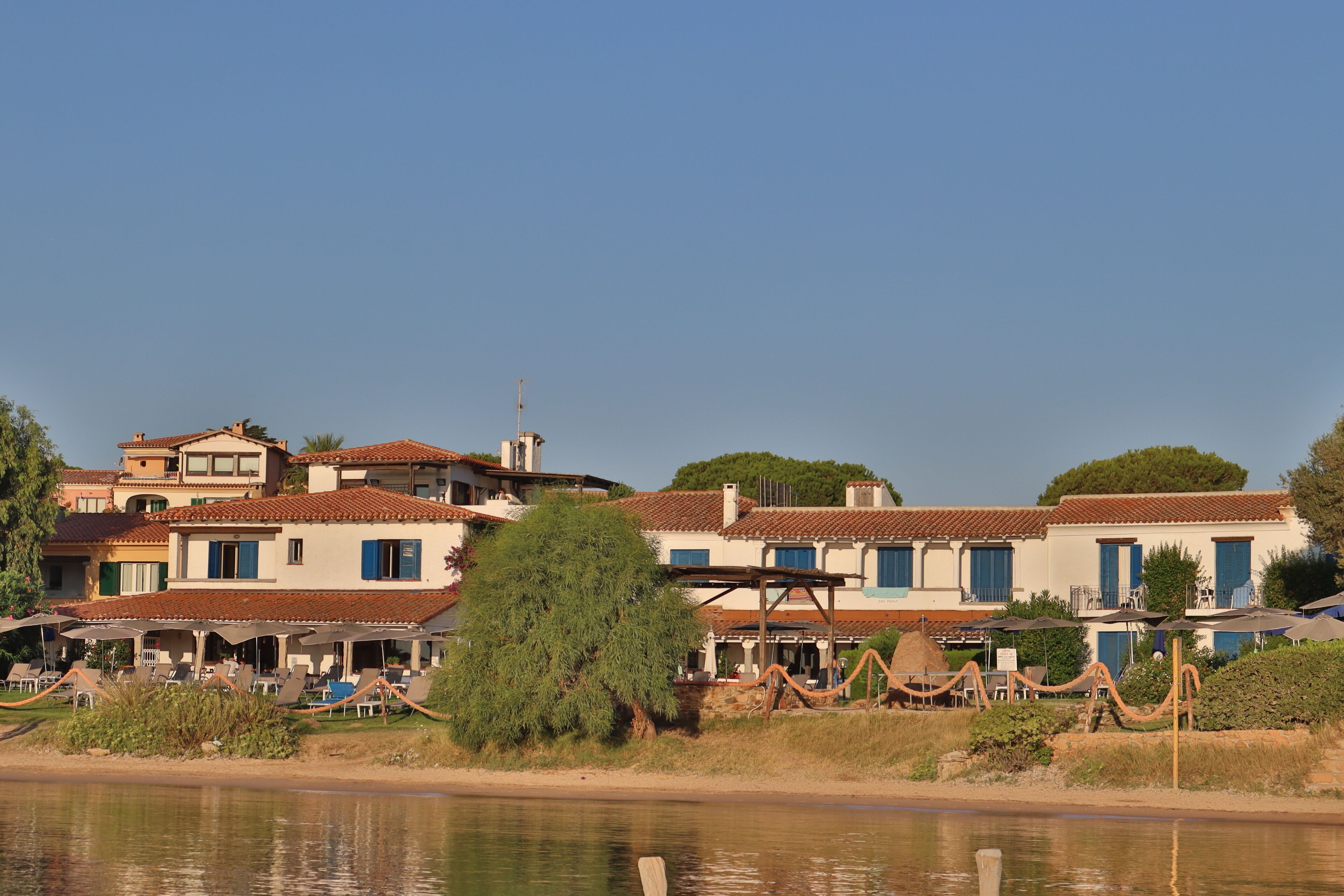 A coastal hotel with multiple buildings, outdoor seating, and a view of the sea.