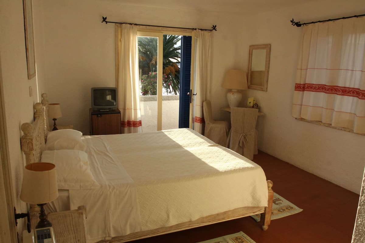 Une chambre à coucher avec un lit, une télévision, une chaise, un bureau et une fenêtre avec des rideaux.