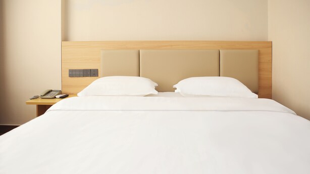 A neatly made bed with a wooden headboard and a bedside table with a phone and a lamp. - Green Oasis Hotel (Shenzhen)