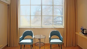 A room with a large window, two chairs, a small table, and a kettle on a shelf. - Green Oasis Hotel (Shenzhen)