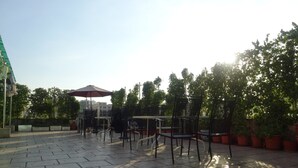 An outdoor patio with stone flooring, metal chairs, and tables, surrounded by potted plants and trees. - Green Oasis Hotel (Shenzhen)