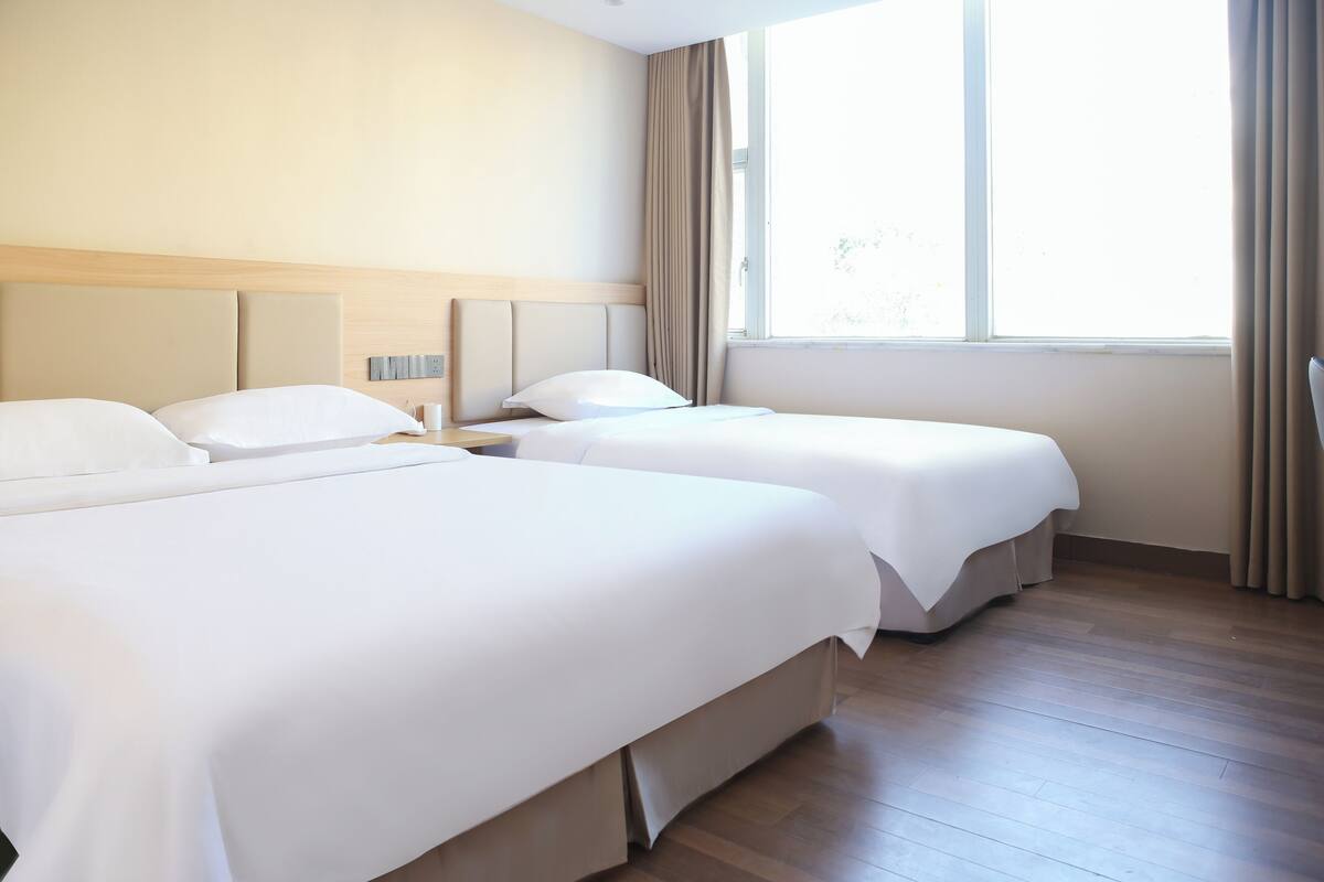 A hotel room with two beds, a wooden floor, and a large window with curtains.