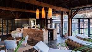 Amplio espacio interior con techo de madera, mostrador de recepción, asientos y ventanas grandes con vistas al exterior.