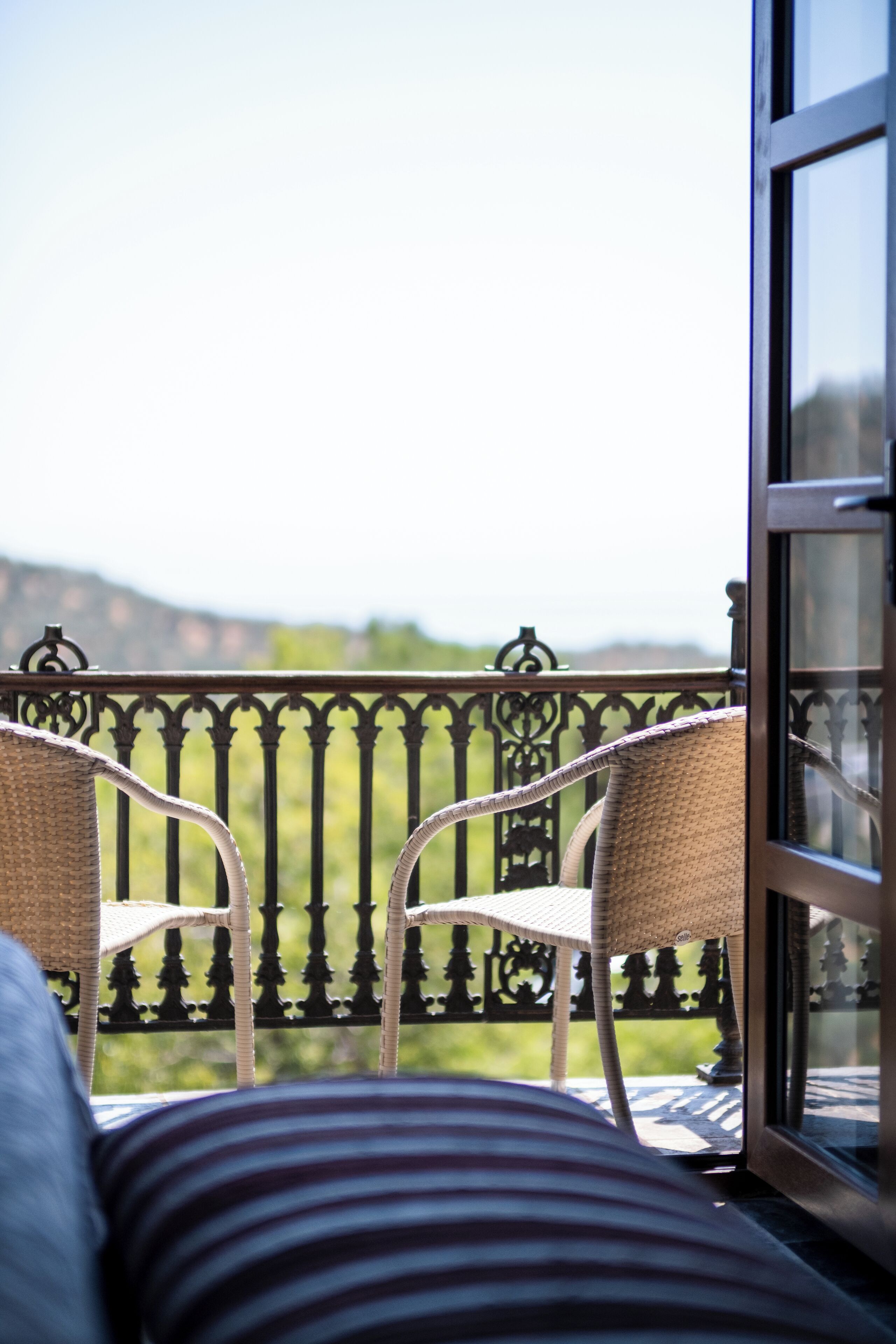 A balcony with wicker chairs and a view of a green landscape.