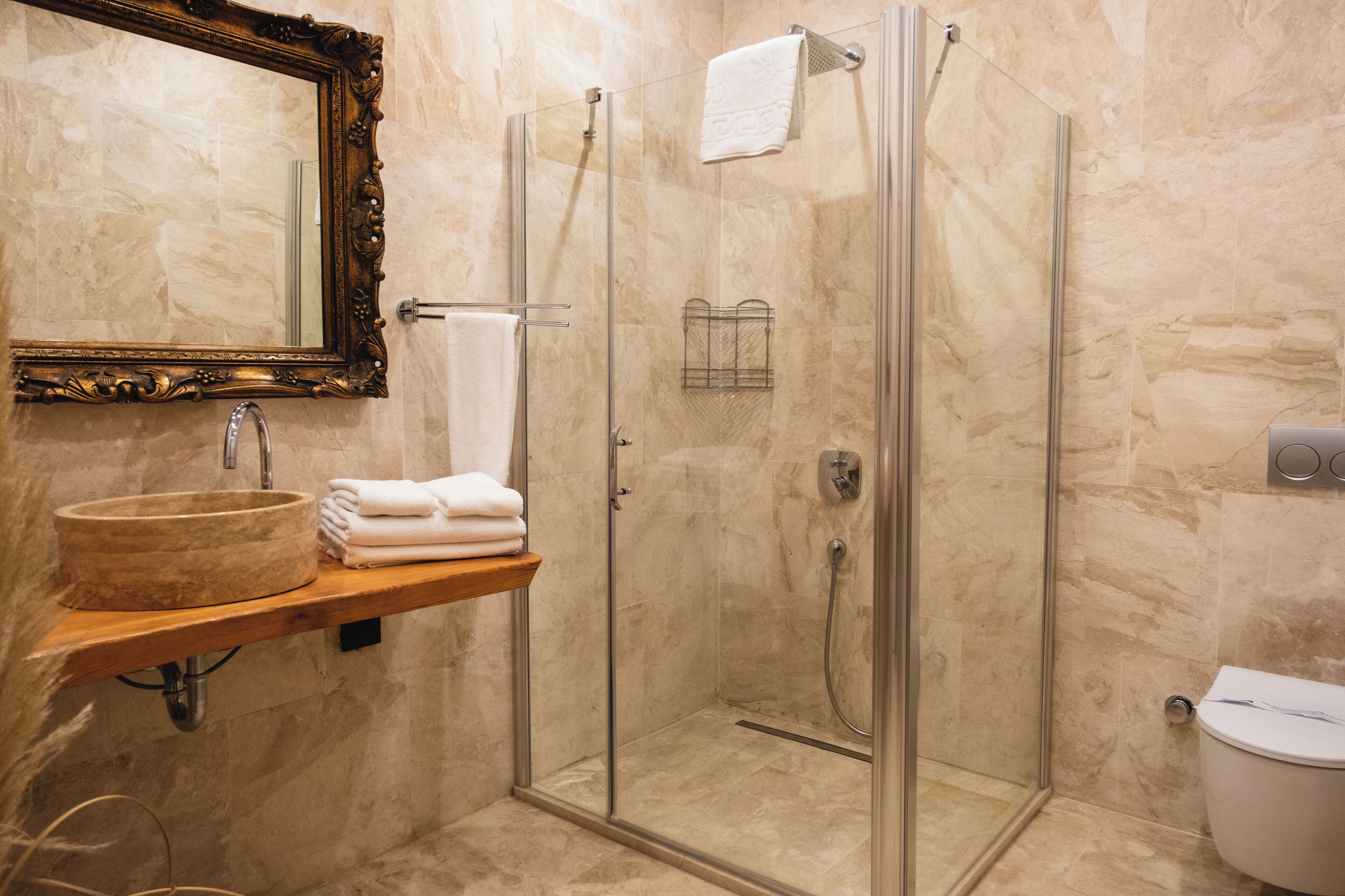 Un bany amb un lavabo de marbre, dutxa amb envidriera i una estantània de fusta amb tovalloles.