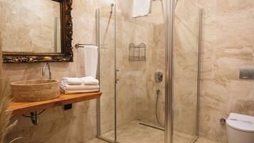 Un bany amb un lavabo de marbre, dutxa amb envidriera i una estantània de fusta amb tovalloles.