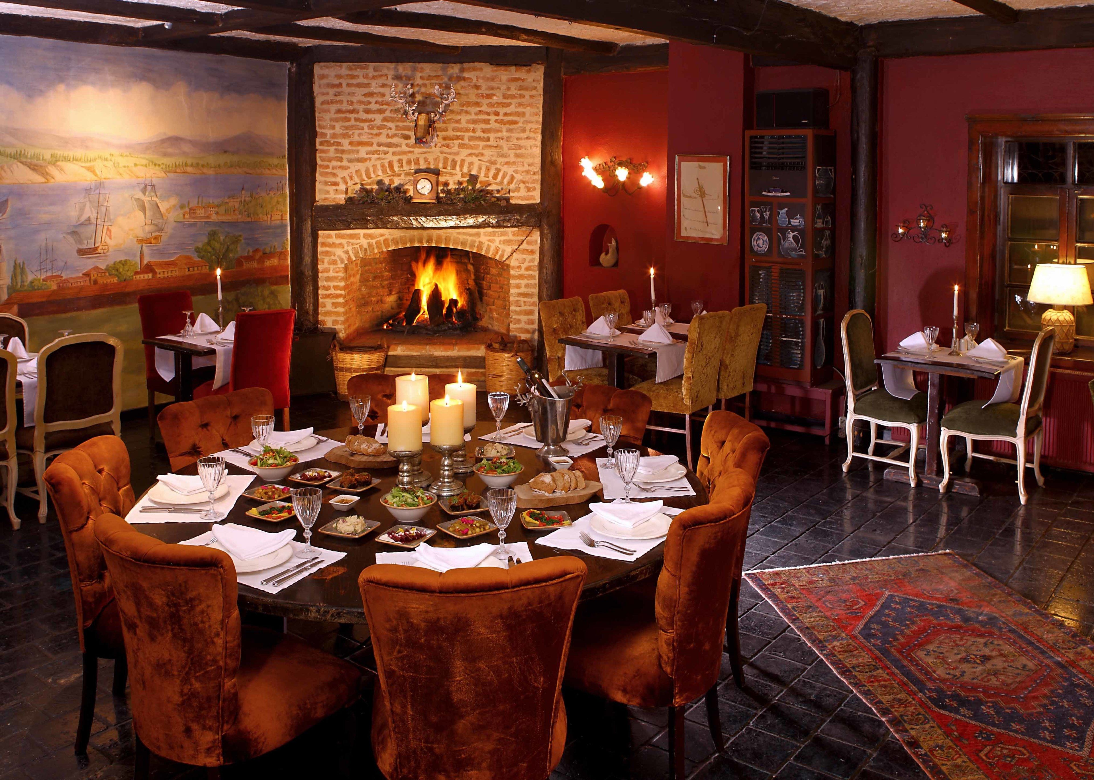 A dining room with a brick fireplace, red walls, and a large dining table set for six.