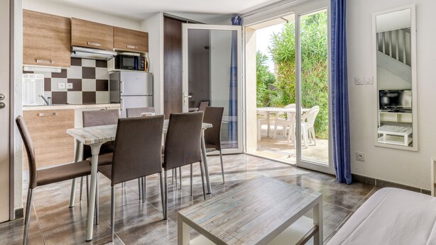 Une cuisine moderne équipée d’un four à micro-ondes, d’un réfrigérateur et d’un crédence à carreaux. On y trouve également un coin repas avec une table et des chaises, ainsi qu’une porte-fenêtre coulissante donnant sur une terrasse aménagée avec du mobilier d’extérieur.