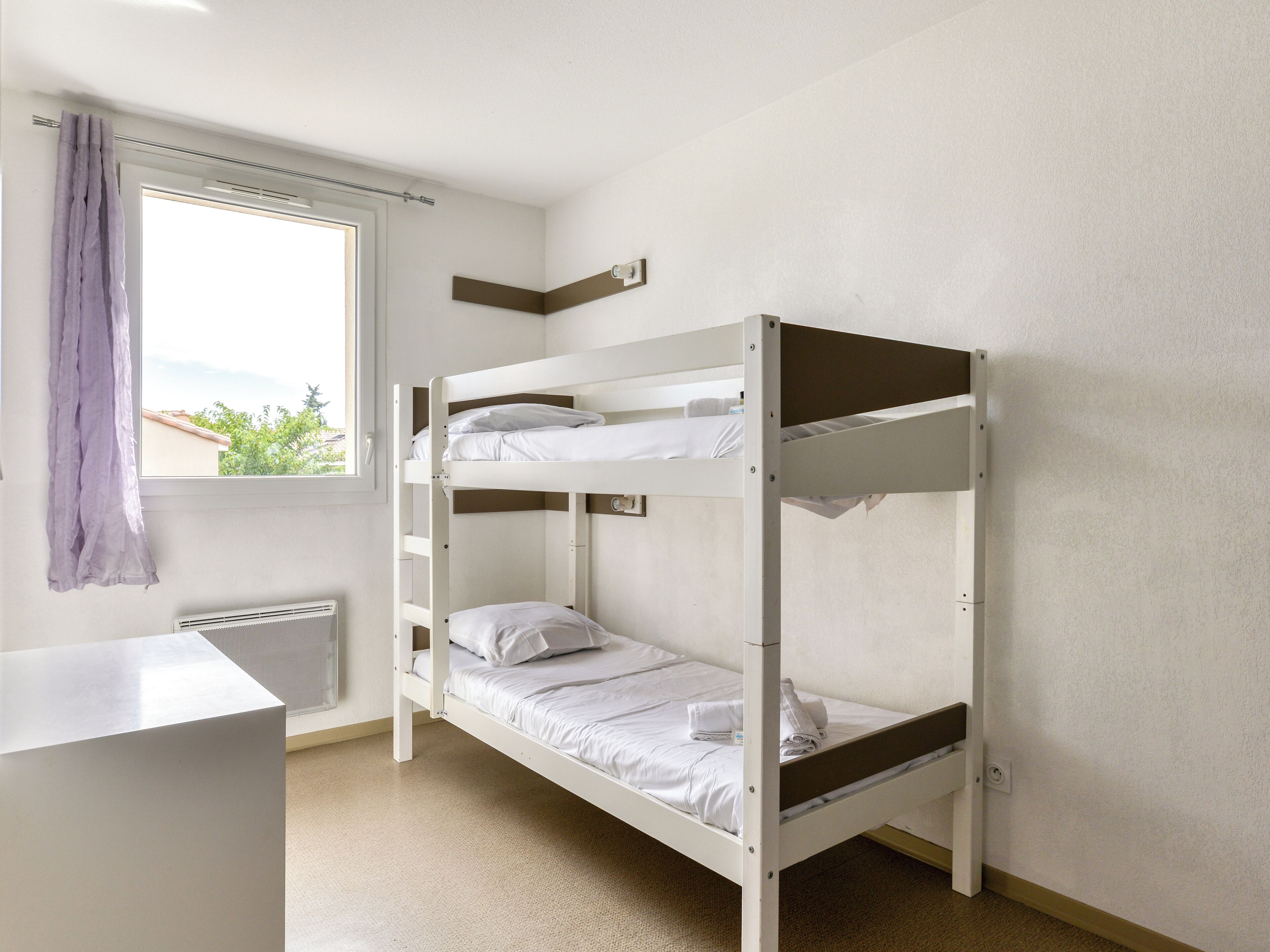 A bunk bed room with a window, a radiator, and a desk.