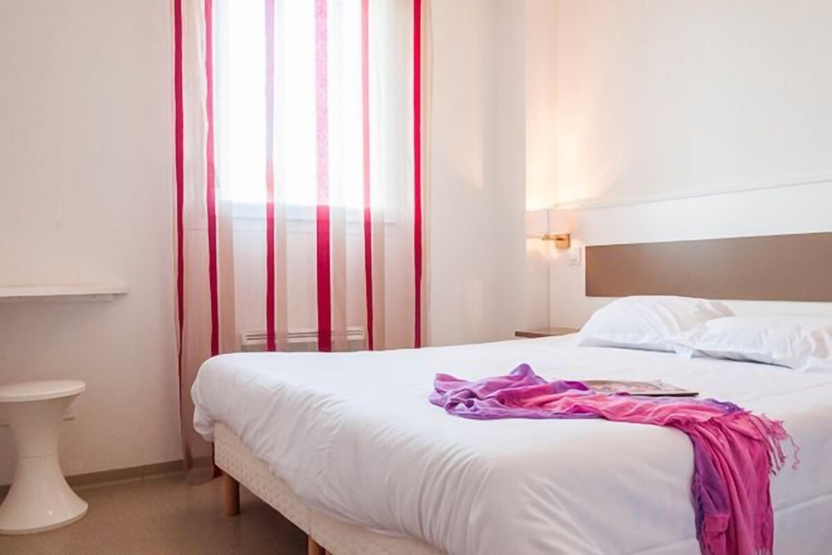 Une chambre d’hôtel avec un lit, une table de chevet, une commode et une fenêtre avec des rideaux.