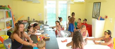 Un aula con niños realizando actividades, mesas, sillas y material educativo.