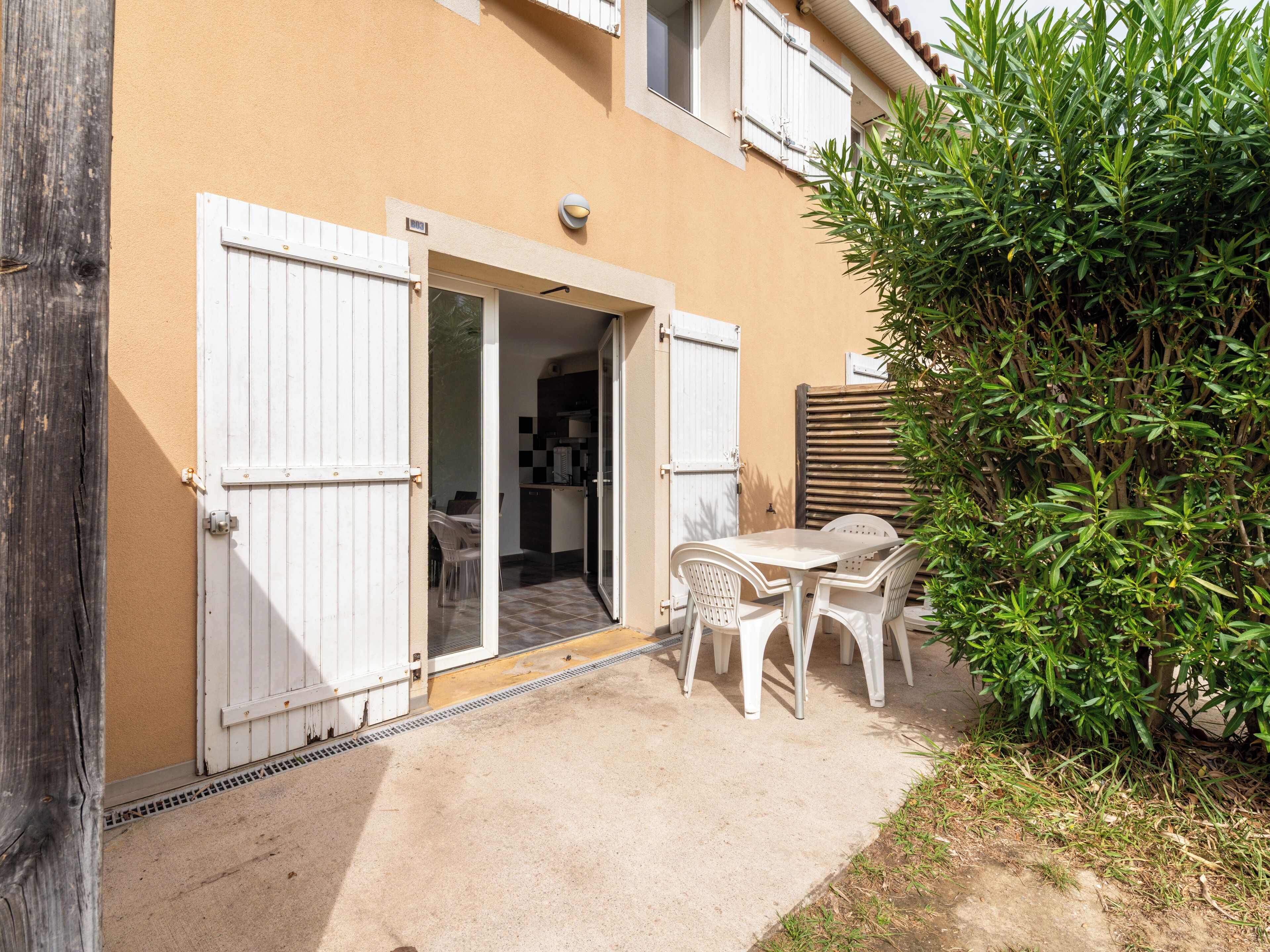 Un pequeño patio exterior con una mesa y sillas, una cerca de madera y una puerta que da a un espacio interior.