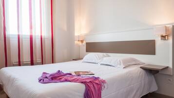 Una habitación de hotel con una cama grande, ropa de cama blanca, cabecera, lámparas de noche y una ventana con cortinas.