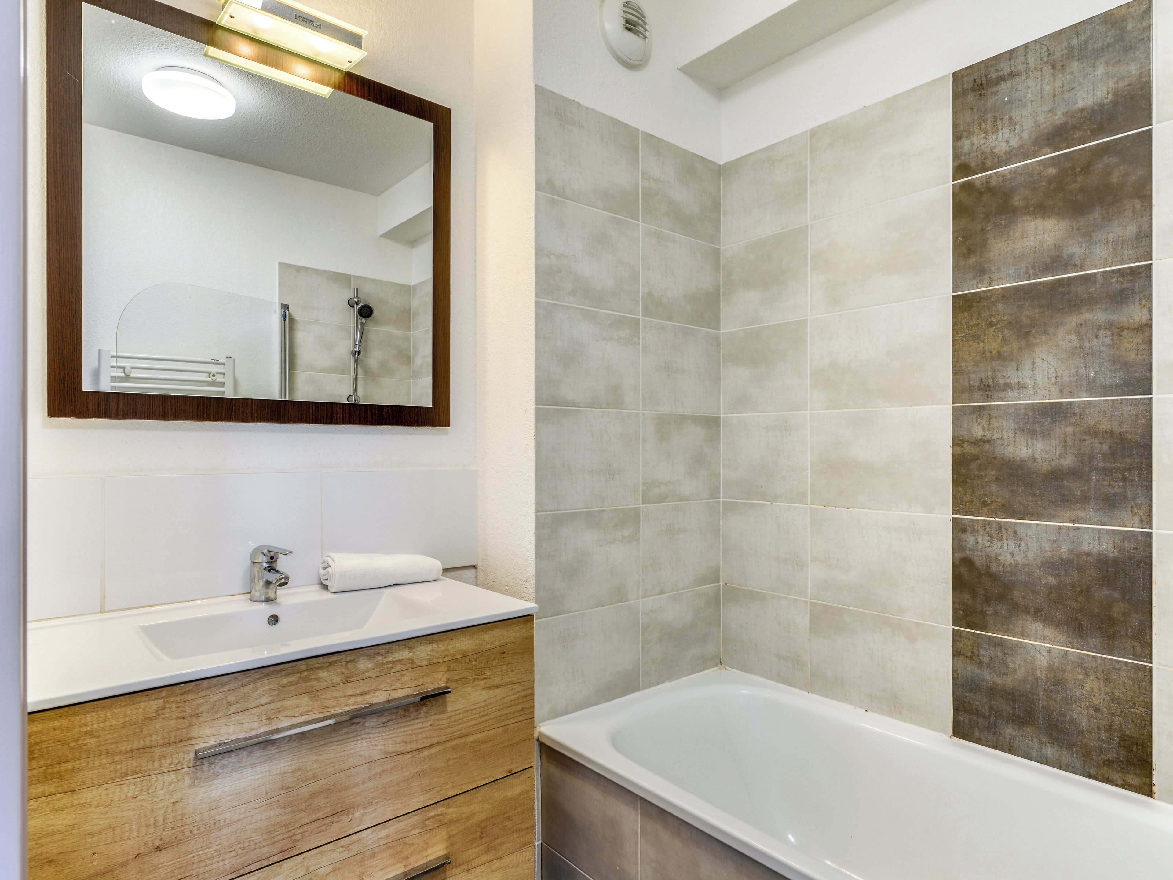 Ein Badezimmer mit einer weißen Badewanne, einem hölzernen Waschtisch mit Spiegel und gefliesten Wänden.