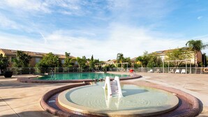 Une piscine avec un jacuzzi, entourée d’une terrasse carrelée et d’une clôture.