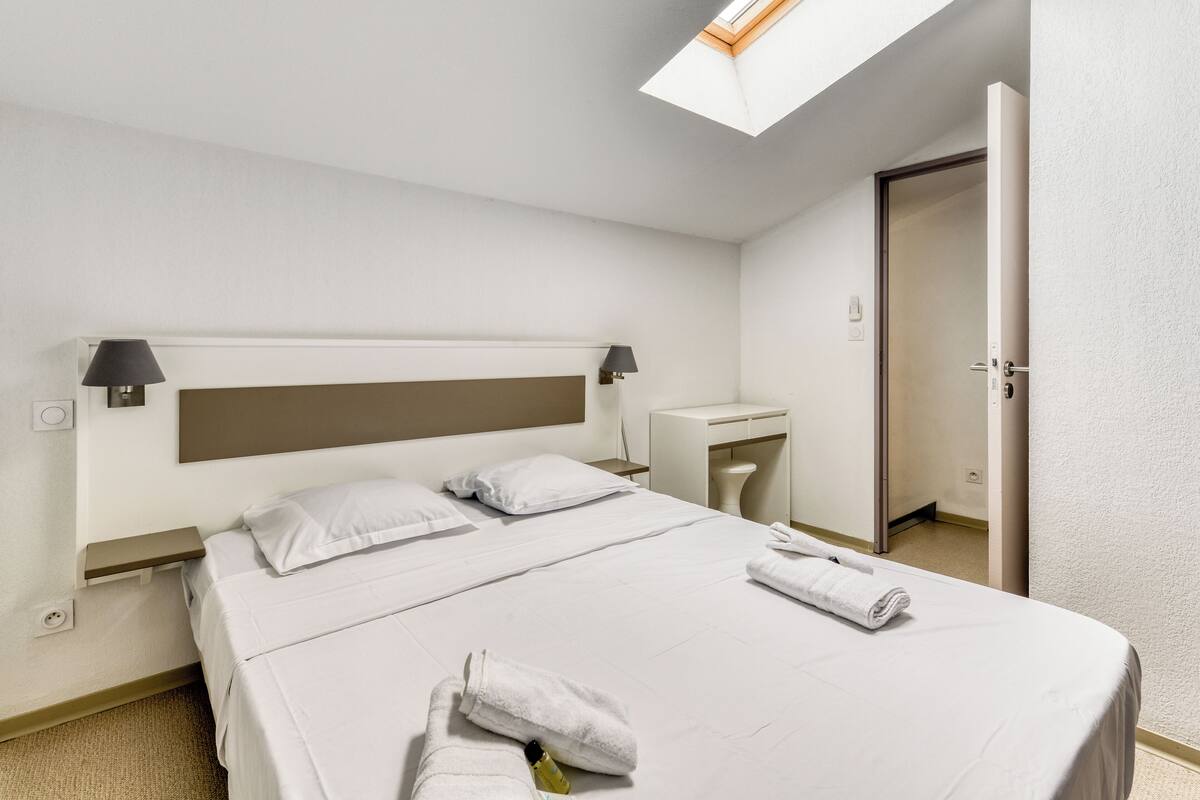 Ein Hotelzimmer mit Bett, Nachttischen, Schreibtisch, Toilette und einem Dachfenster.