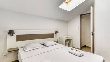 Habitación de hotel con una cama grande, un escritorio, una silla y un tragaluz.
