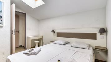 A hotel room with a bed, bedside tables, a desk, a lamp, and a skylight.