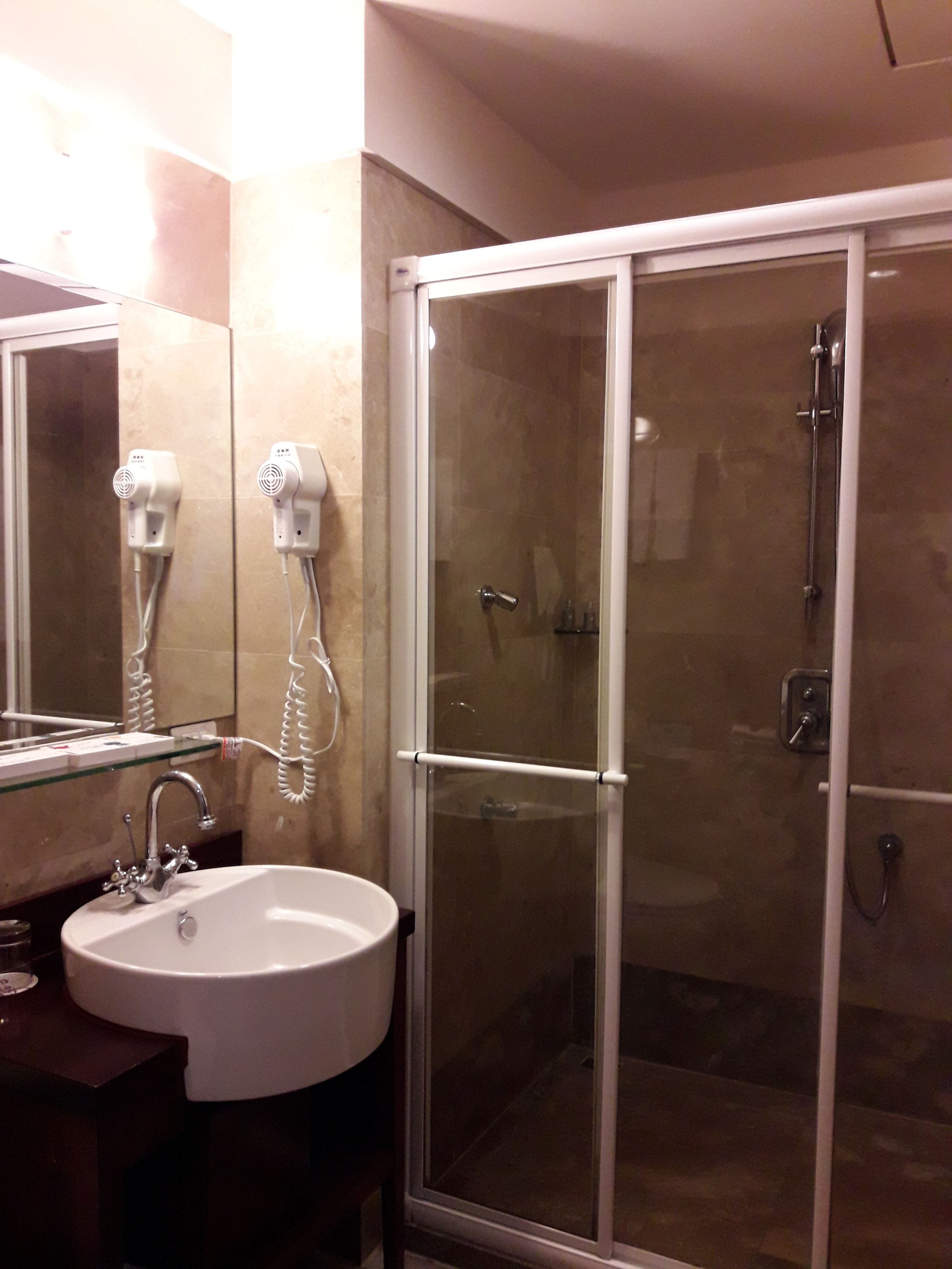 Une salle de bain dotée d’une douche à parois de verre, d’un lavabo avec un miroir et de deux sèche-cheveux fixés au mur.