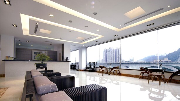 Een moderne hotellobby met een lange receptiebalie, een zithoek met banken en stoelen, grote ramen met uitzicht op een stadsbeeld en een rivier.