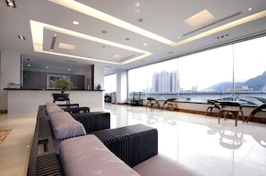 A modern hotel lobby with a long reception desk, seating area with sofas and chairs, large windows offering a view of a cityscape and a river. - Beautiful Hotel Taipei (New Taipei City)