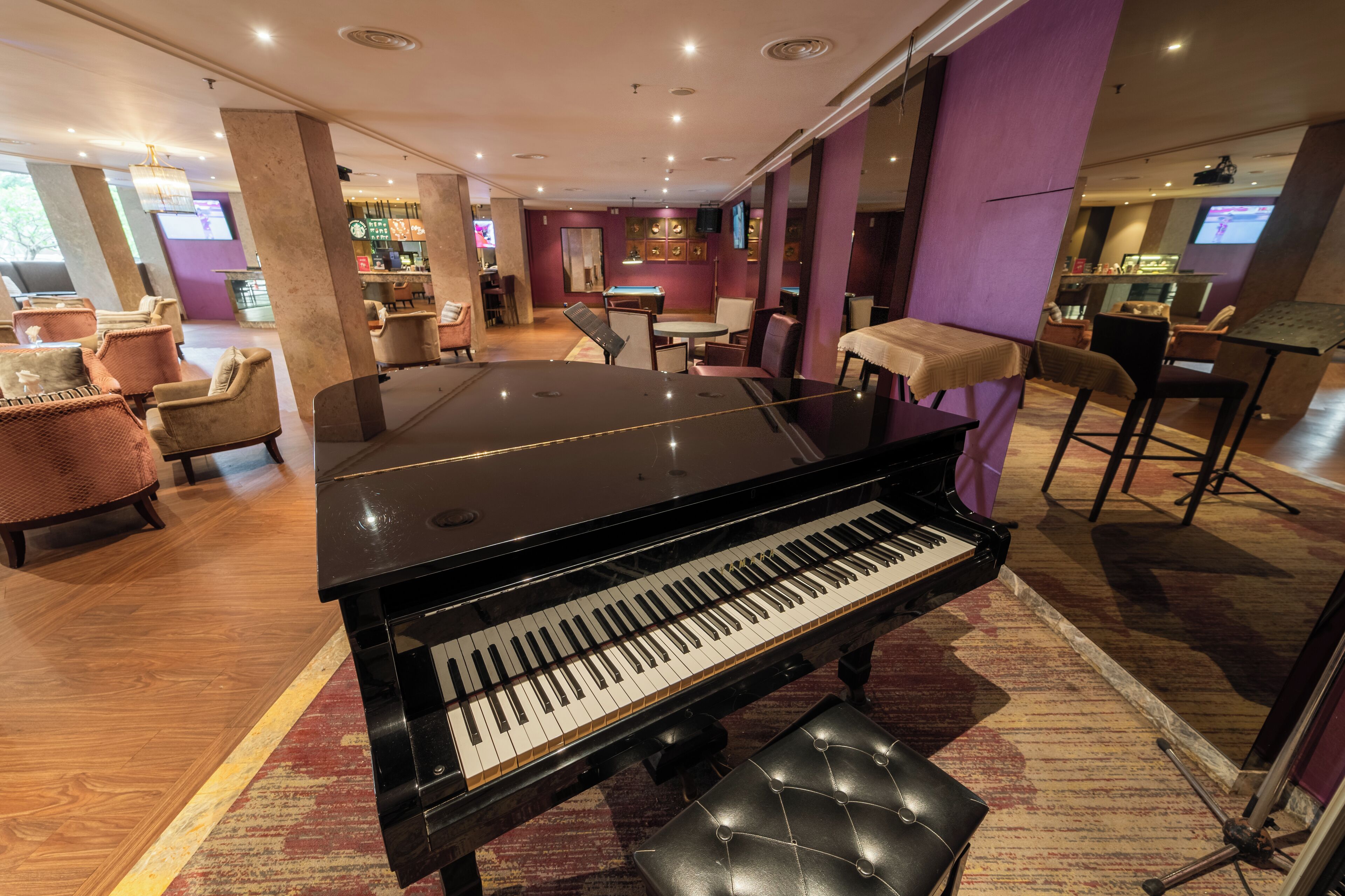 A grand piano in a hotel lobby with seating and a bar area.