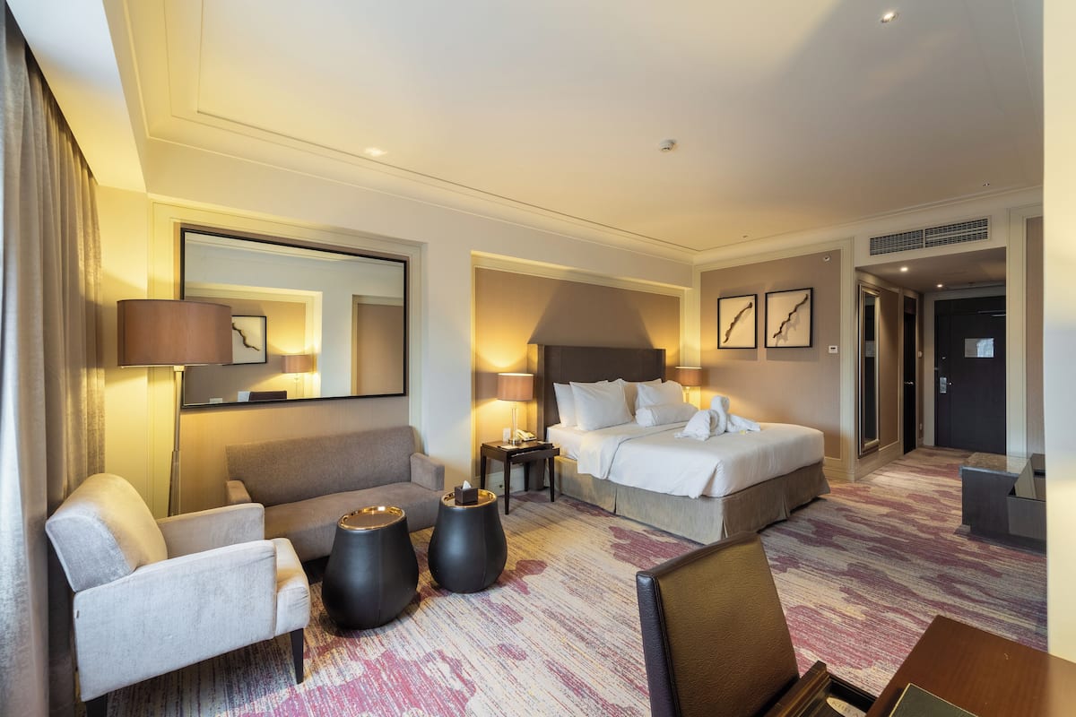 A hotel room with a bed, a sofa, a chair, two side tables, and a large mirror.