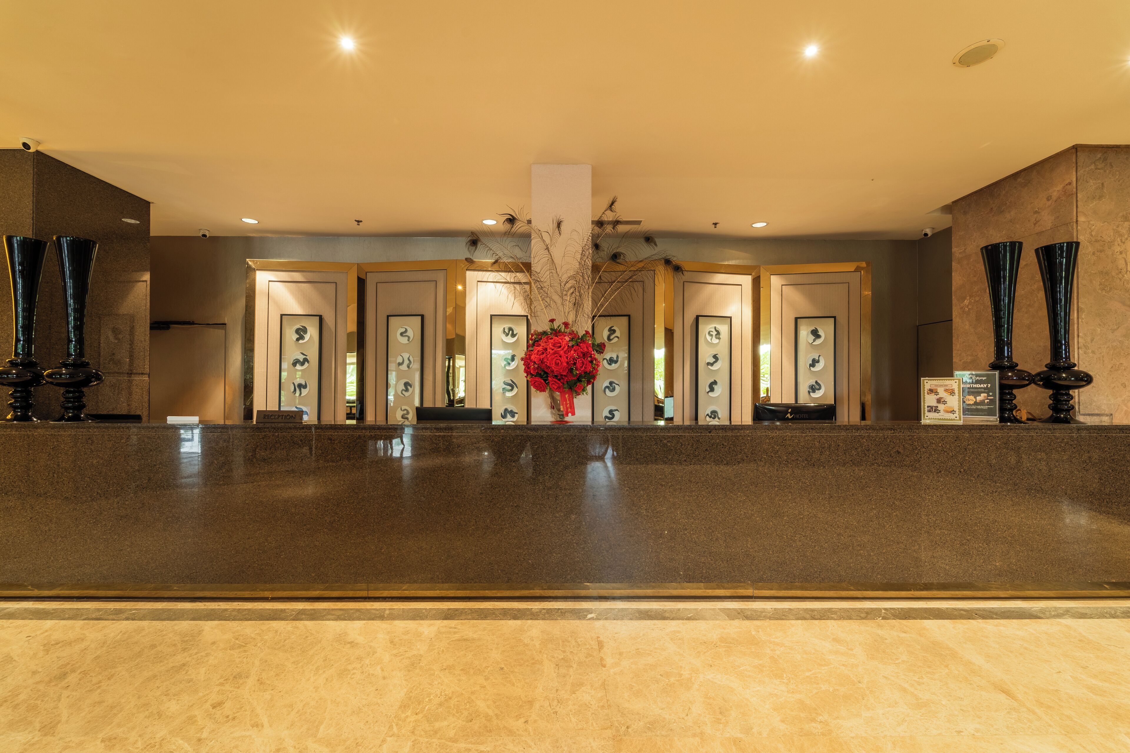 A reception area with a marble counter, framed artwork, and a central vase with red flowers.
