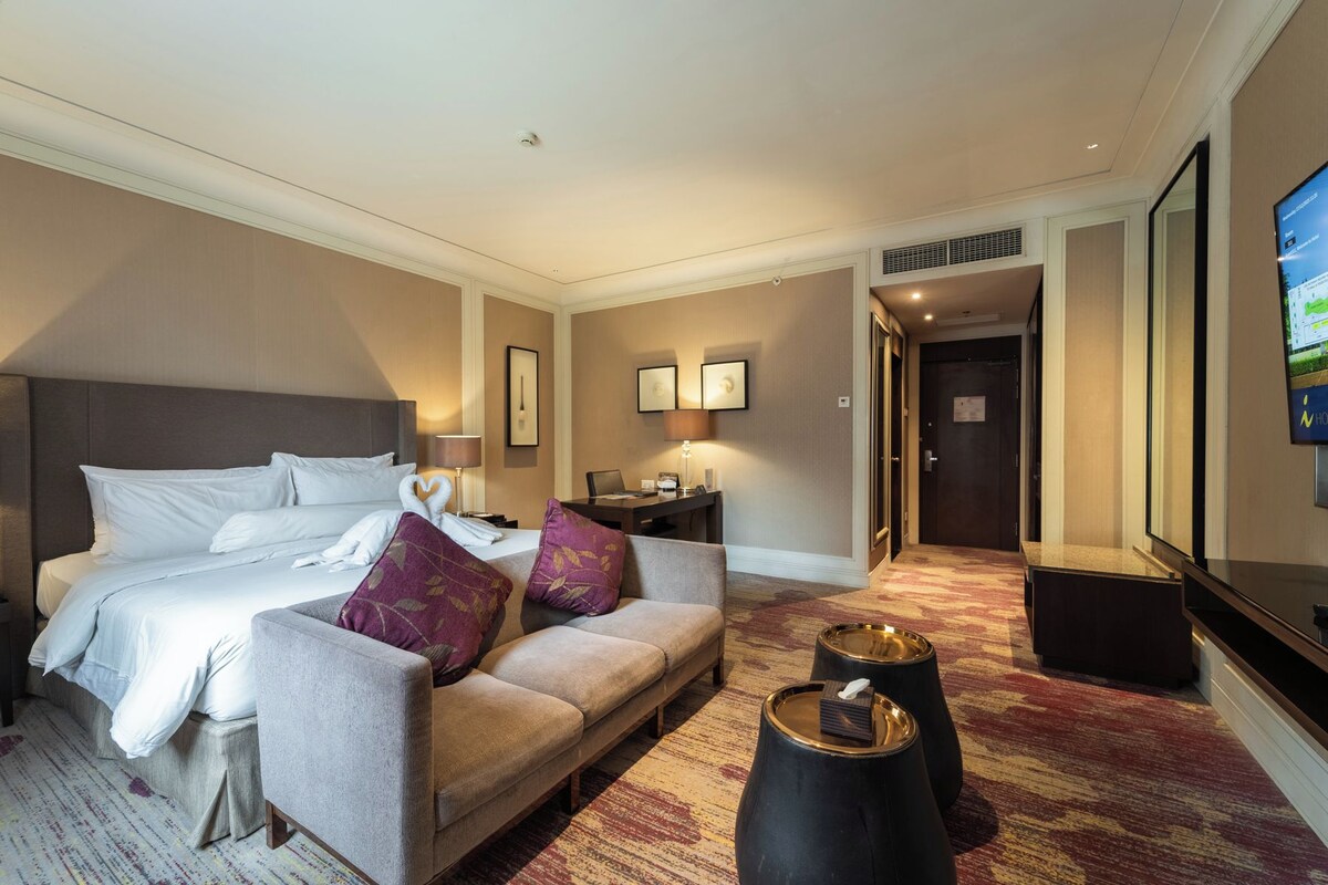 A hotel room with a bed, a sofa, a coffee table, a desk, and a television.