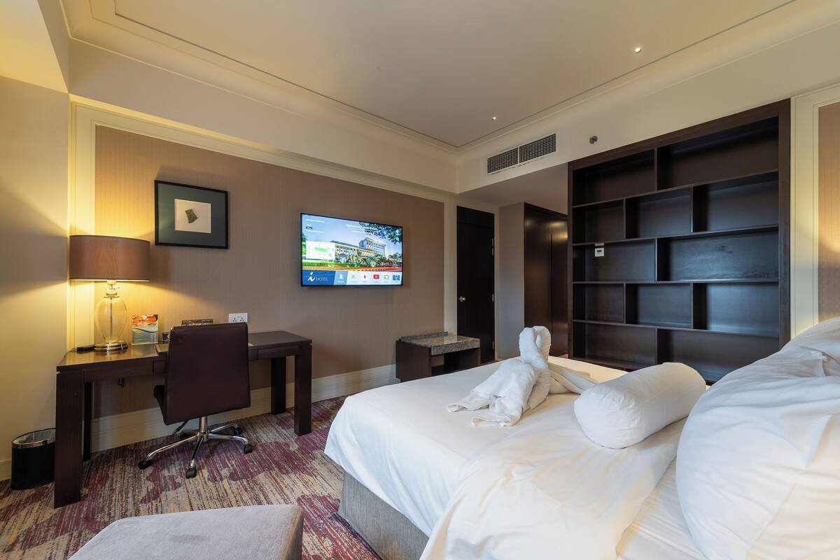 A hotel room with a bed, a desk with a chair, a television, and a built-in shelving unit.