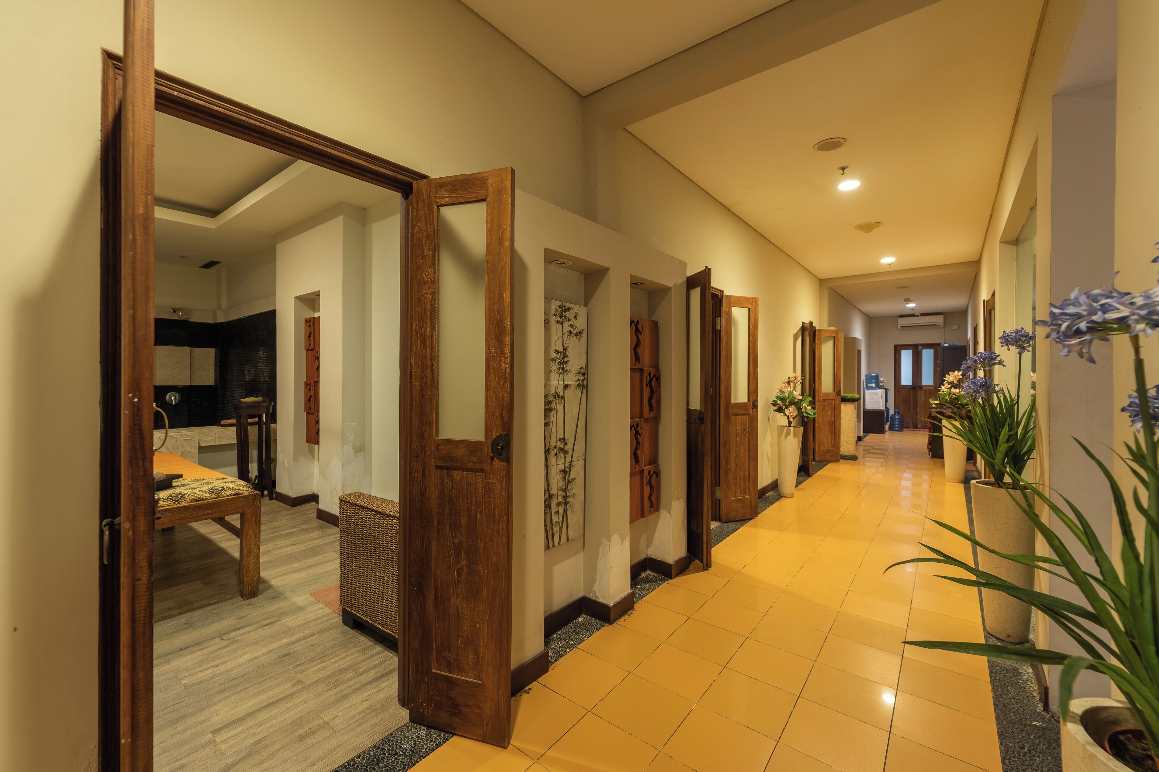 A hallway with wooden doors, a tiled floor, and potted plants.