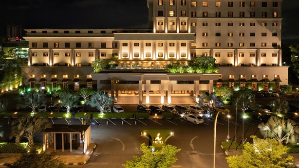 Ein mehrstöckiges Hotel mit gut beleuchteter Fassade, einem Parkplatz und einem kleinen Garten.