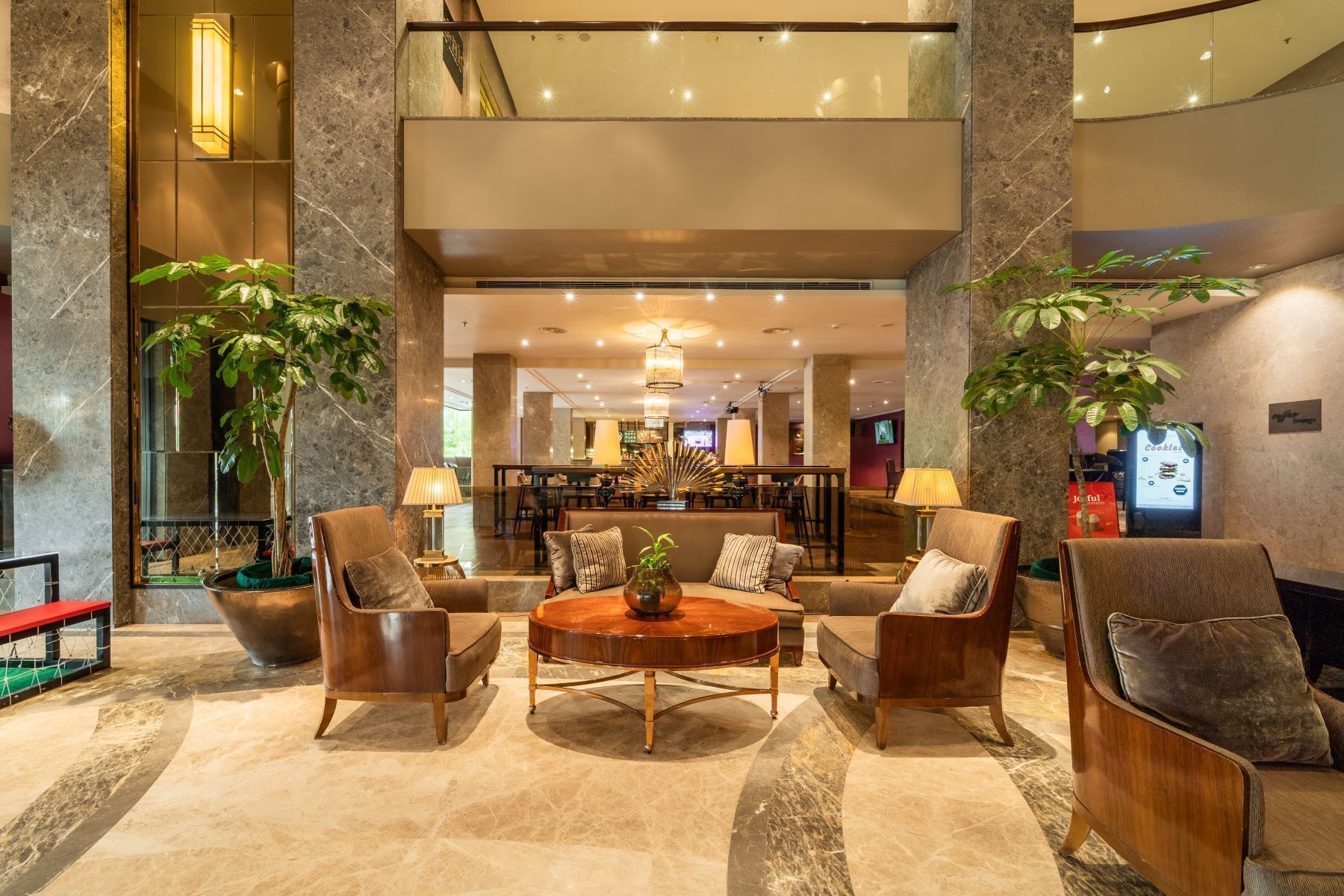 A lobby with a round wooden table, multiple sofas, and large potted plants.