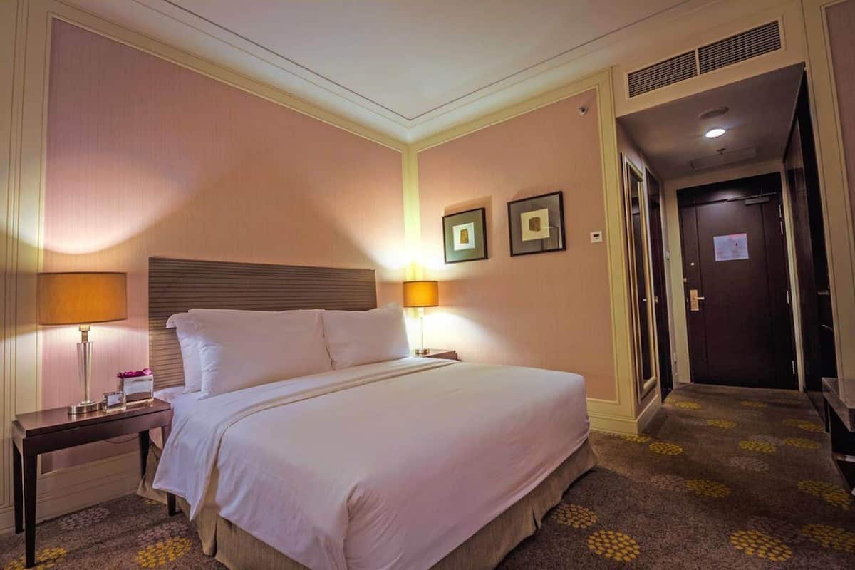 A hotel room with a large bed, two bedside tables, a headboard, a door, and a carpet with a pattern.