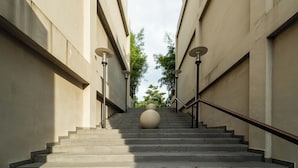 Eine Treppe, deren Spitze von einer großen, kugelförmigen Struktur dominiert wird, gesäumt von Gebäuden mit sichtbaren Fenstern und einem Metallgeländer.