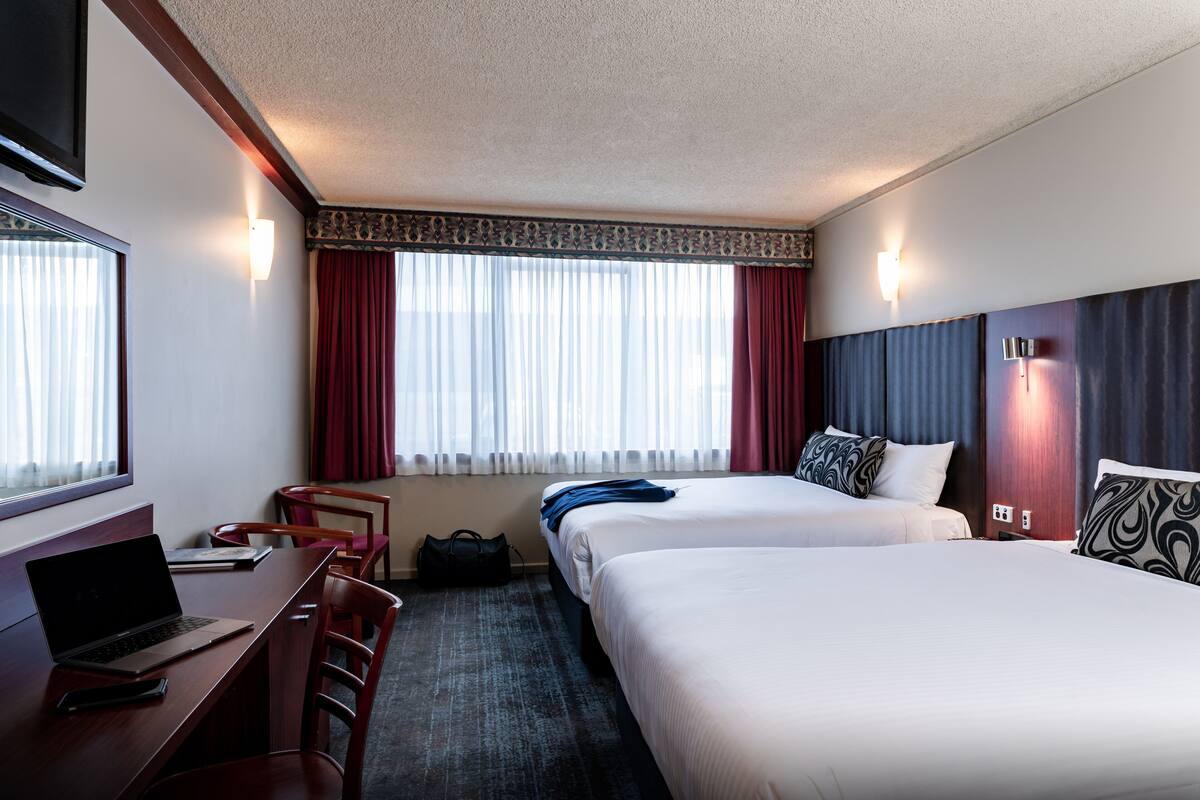 A hotel room with two beds, a desk with a laptop, a chair, and a suitcase.