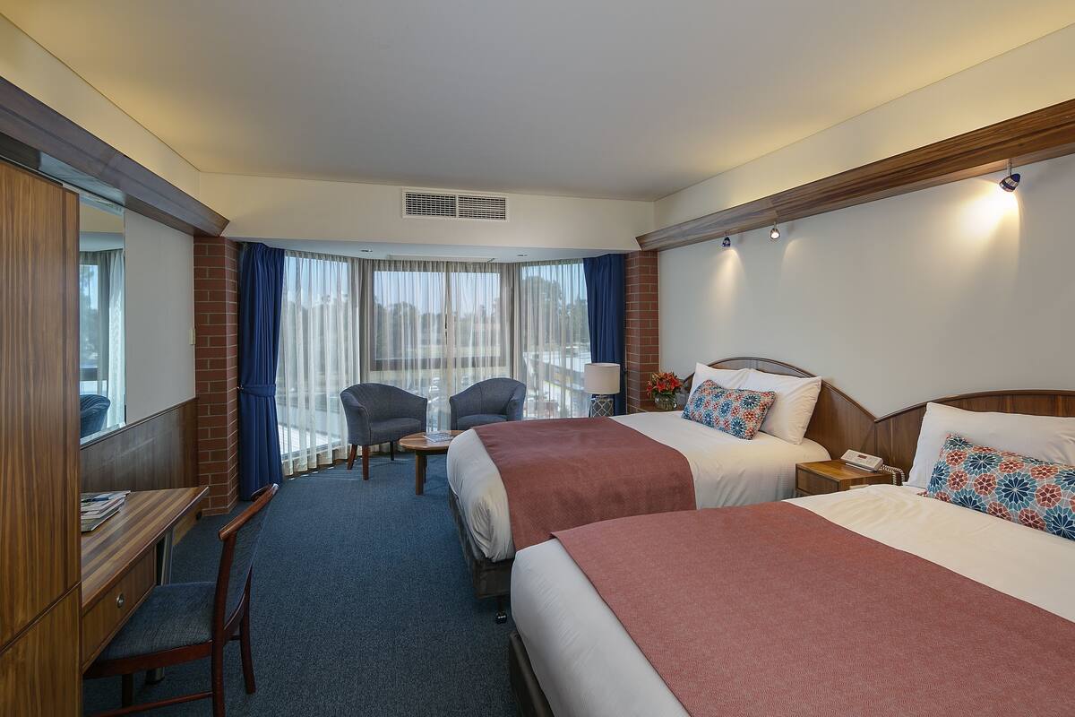 A hotel room with two beds, a desk, and a chair.