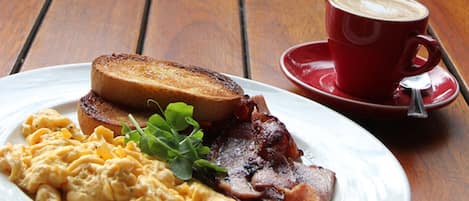 A breakfast plate with toast, scrambled eggs, bacon, and a cup of coffee on a wooden table.