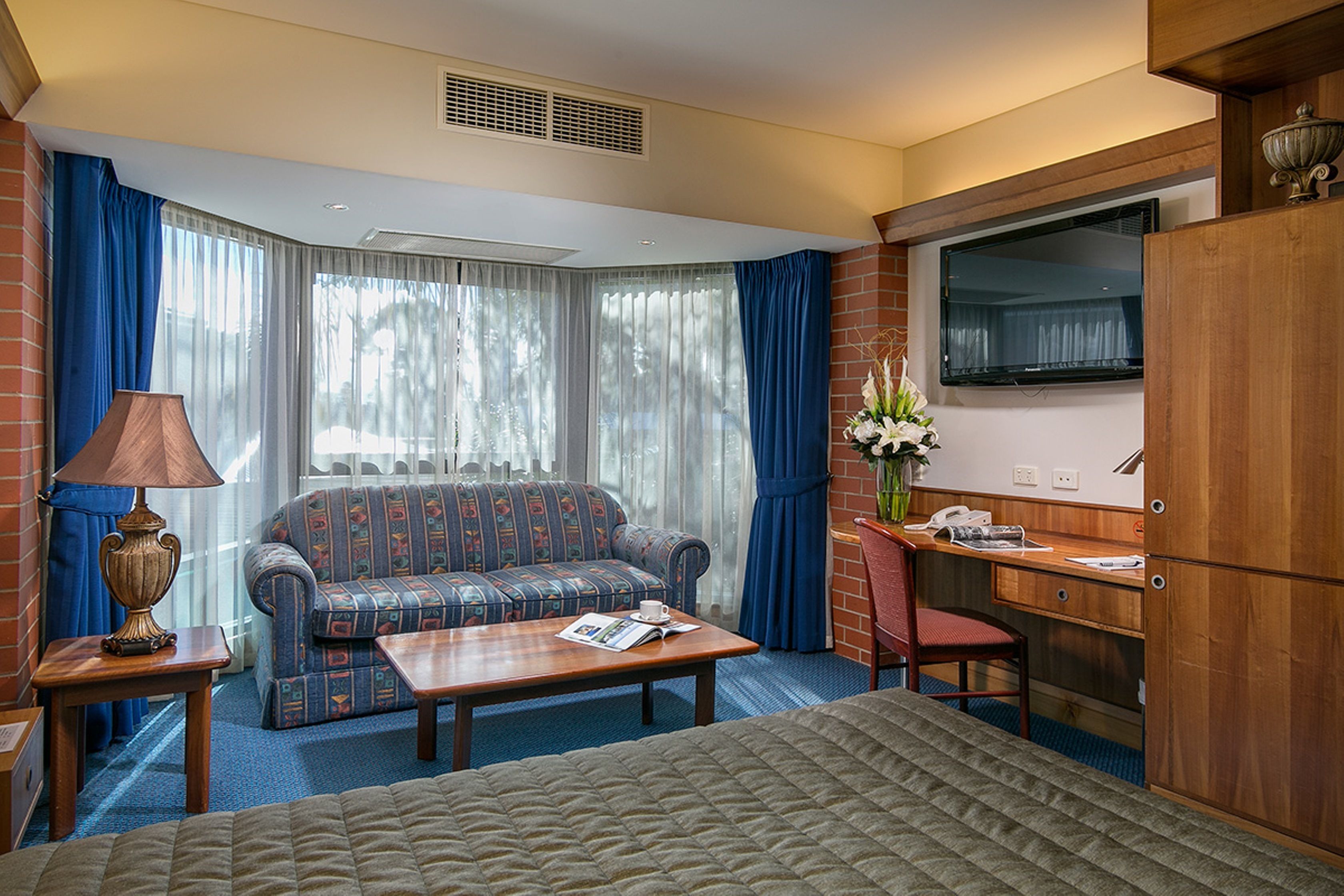 A hotel room with a bed, a sofa, a desk, a lamp, and a TV.
