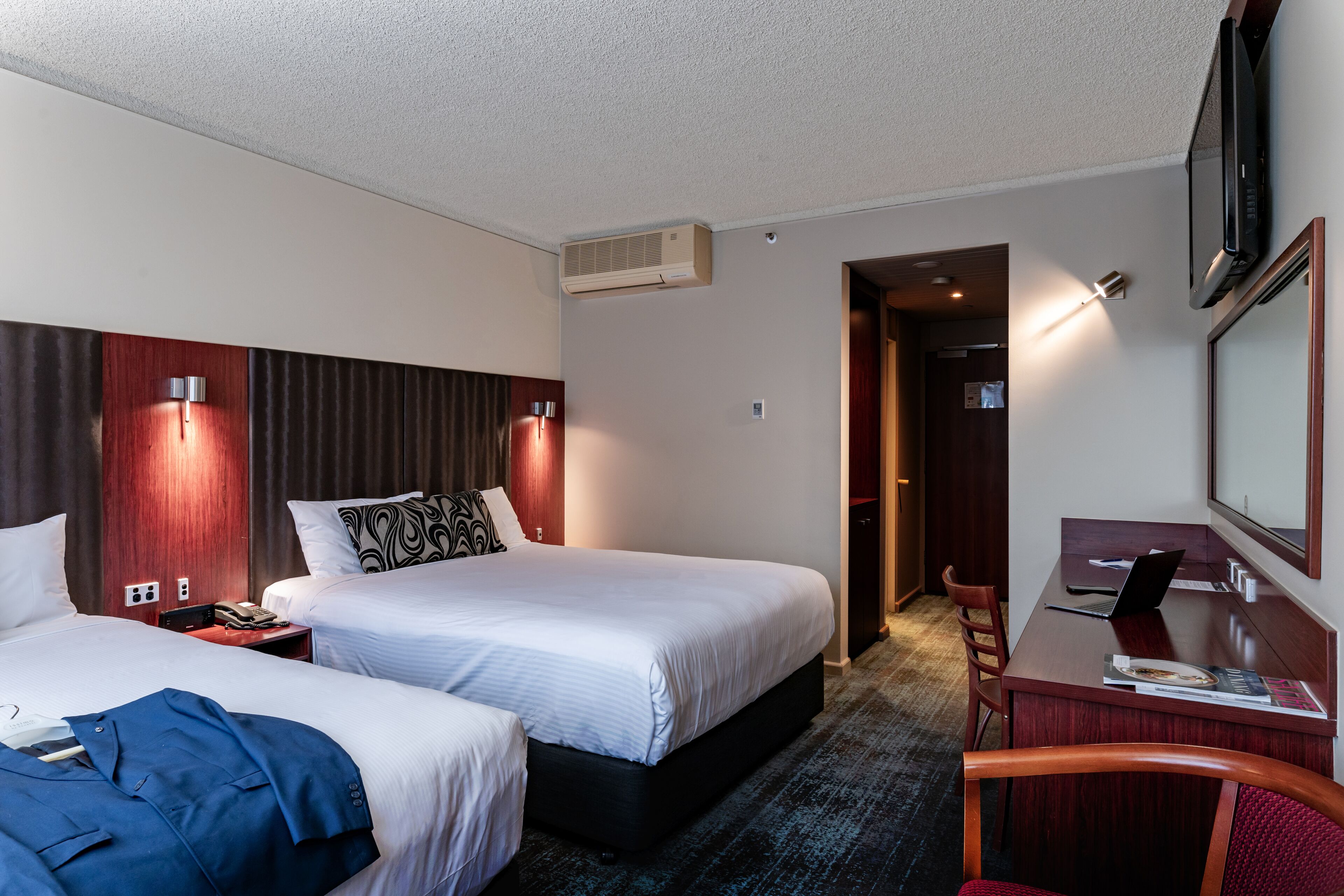Habitación de hotel con dos camas, un escritorio, una silla y un televisor.