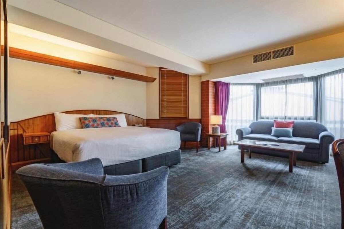 A hotel room with a bed, a sofa, a coffee table, and a chair.