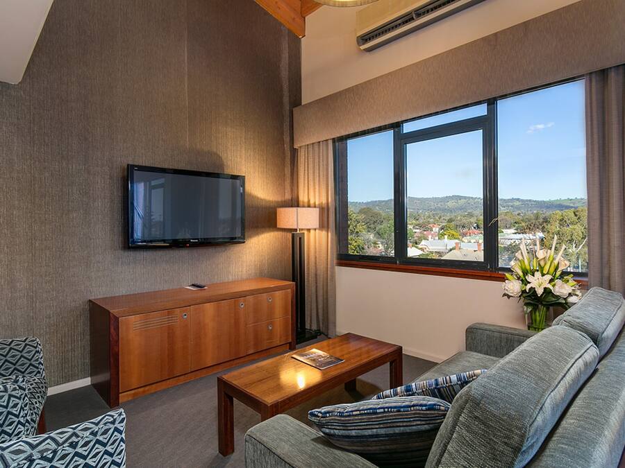 Uma sala de estar moderna com televisão de tela plana, um aparador de madeira, um sofá, uma mesa de centro e uma grande janela com vista para a cidade.