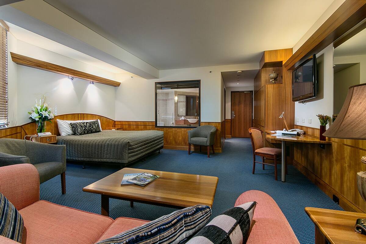 A hotel room with a bed, two sofas, a coffee table, a desk, and a TV.