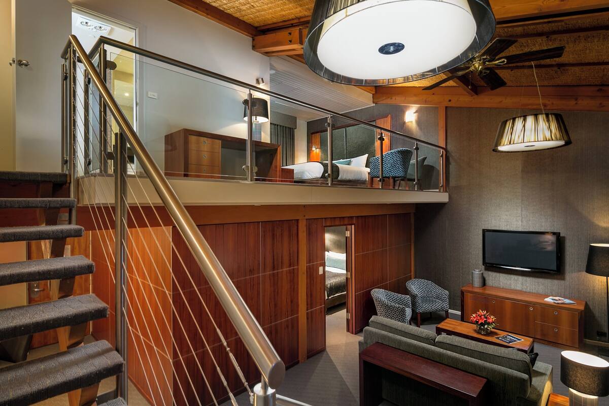 A spacious living area with a high ceiling, a staircase, a balcony, and a television.