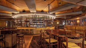 Zona de bar amb barra central, diverses opcions de seients i una varietat de botelles i gots a les prestatgeries.