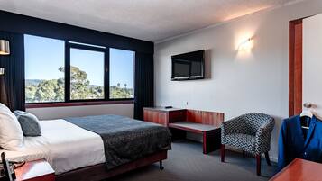 A hotel room with a bed, desk, chair, and a TV on the wall.